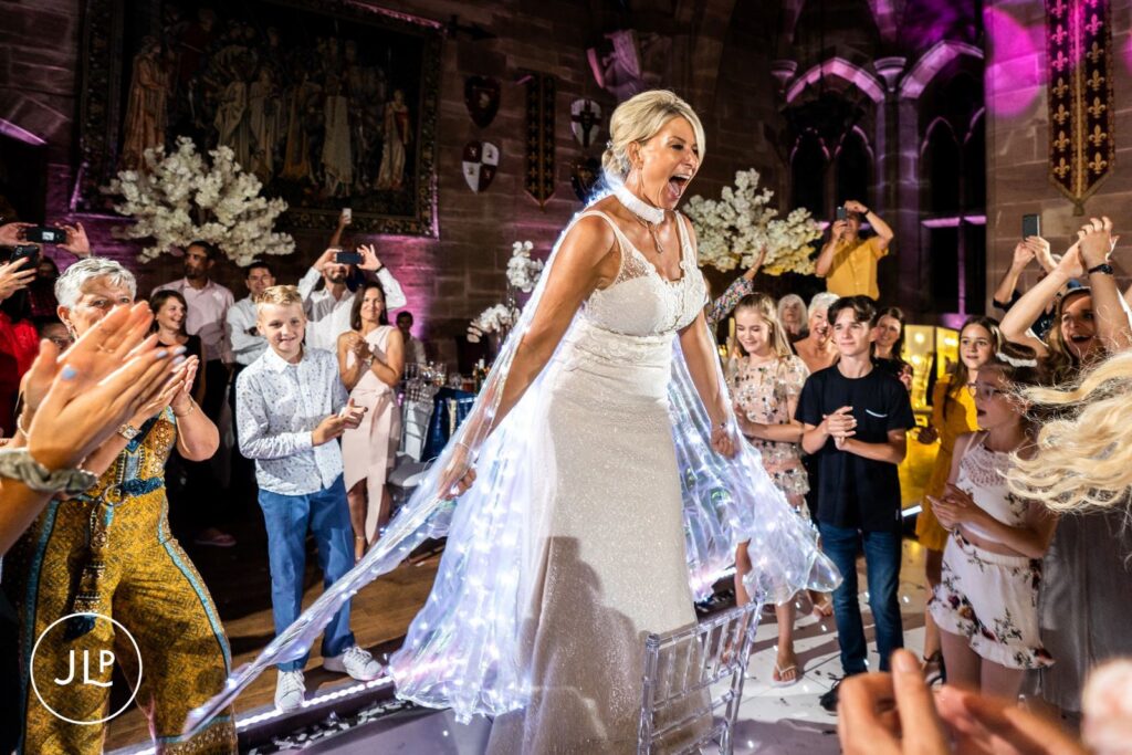 Documentary wedding photography of a bride standing on a chair wearing illuminated LED fairy wings.