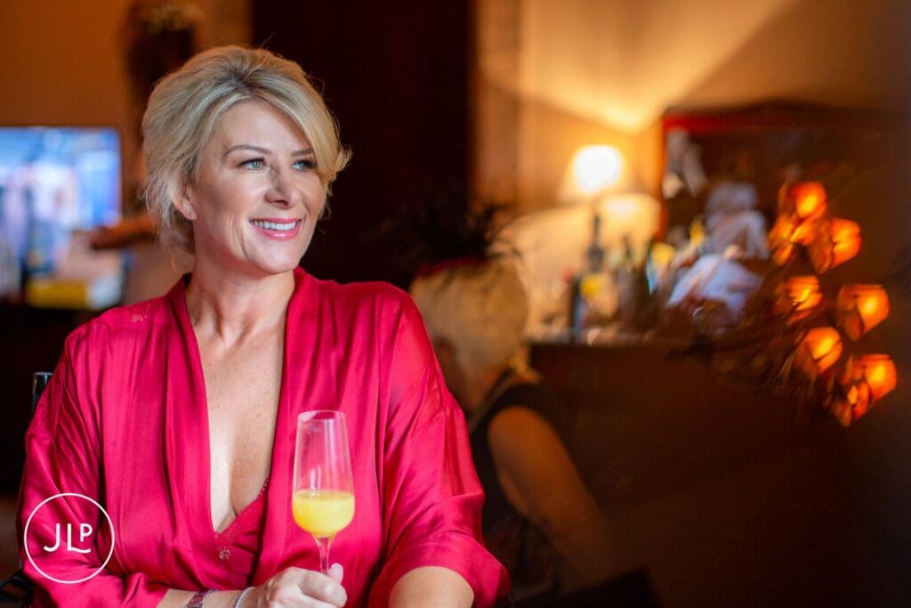 A bride in a red robe holding a champagne glass during relaxed bridal preparations at Peckforton Castle.