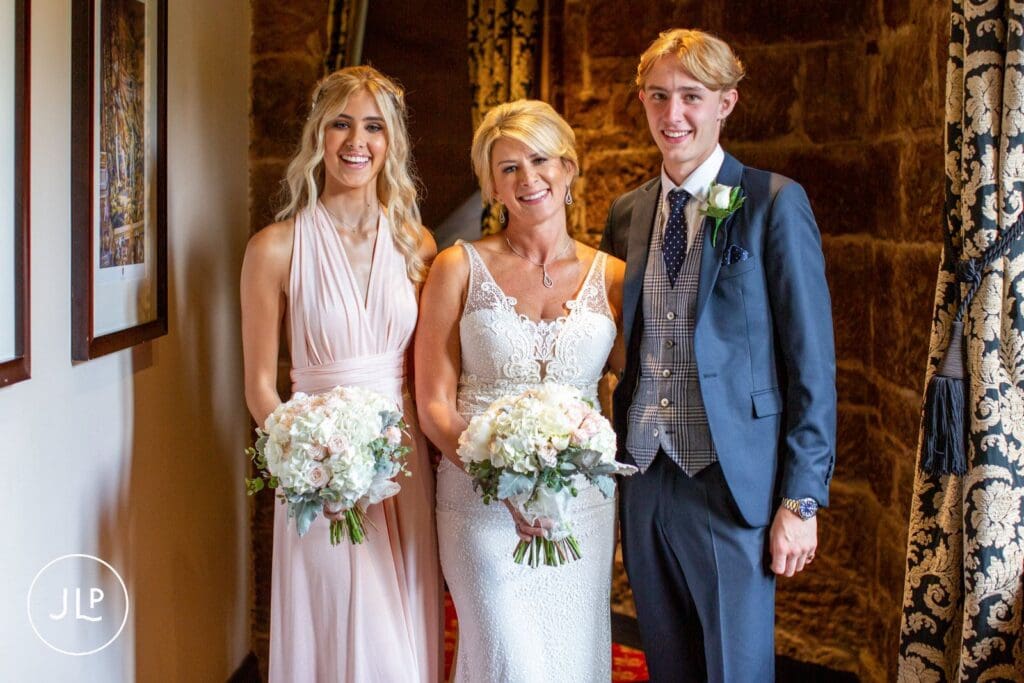 A bride poses with her bridesmaid and groomsman inside an elegant castle wedding venue in Cheshire.