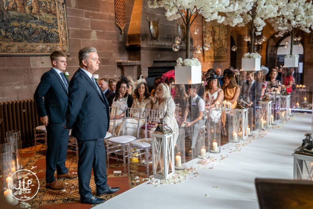 A groom waiting anxiously at the altar during a beautiful Peckforton Castle Cheshire wedding ceremony.