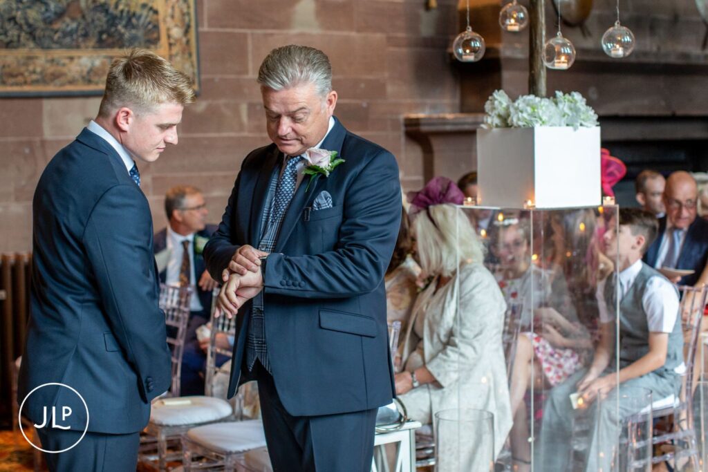 A groom checking his watch during a ceremony captured by a professional Peckforton Castle wedding photographer.