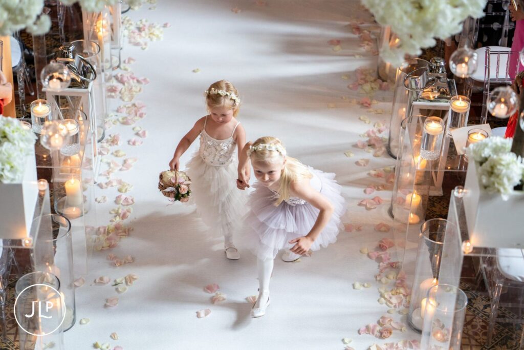 Candid wedding photography of two young flower girls walking down the aisle hand-in-hand.