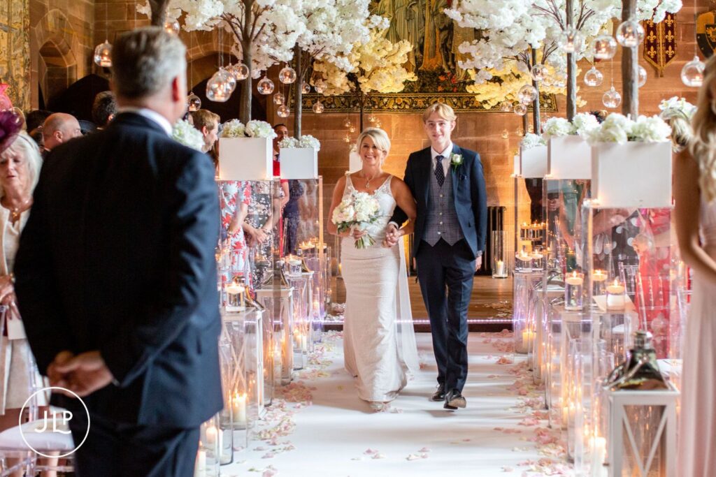 A bride being walked down the aisle by her son during an elegant castle wedding ceremony.