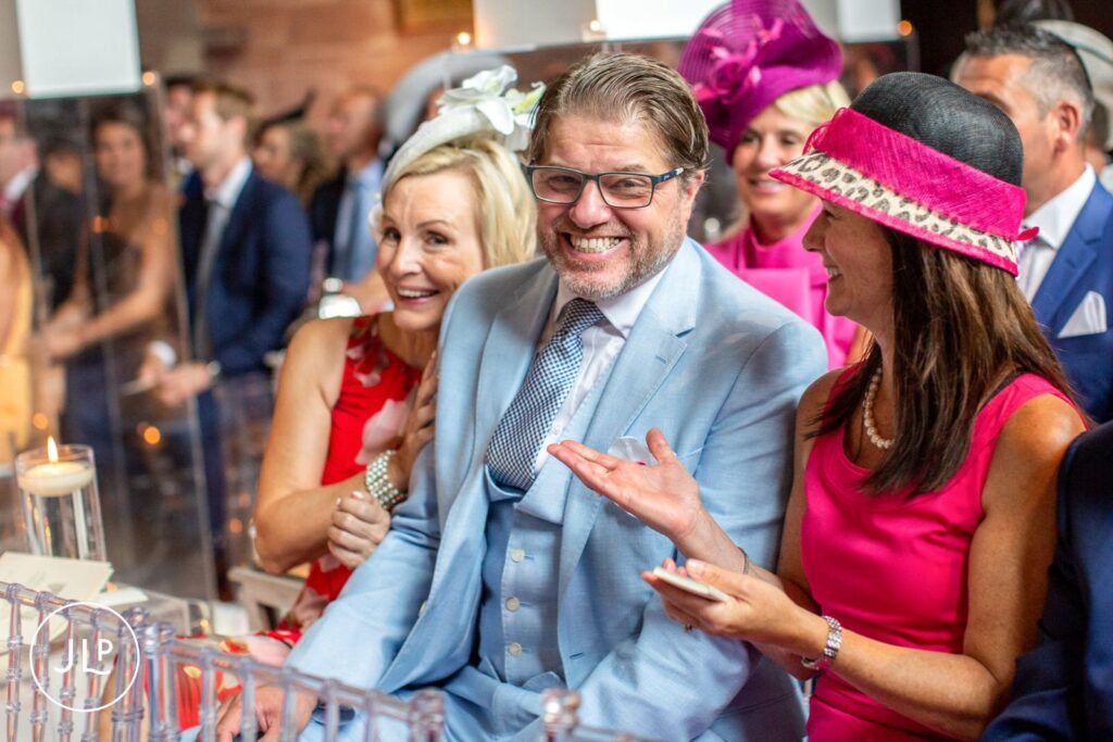 Candid wedding photography of wedding guests laughing in the pews during a Cheshire ceremony.