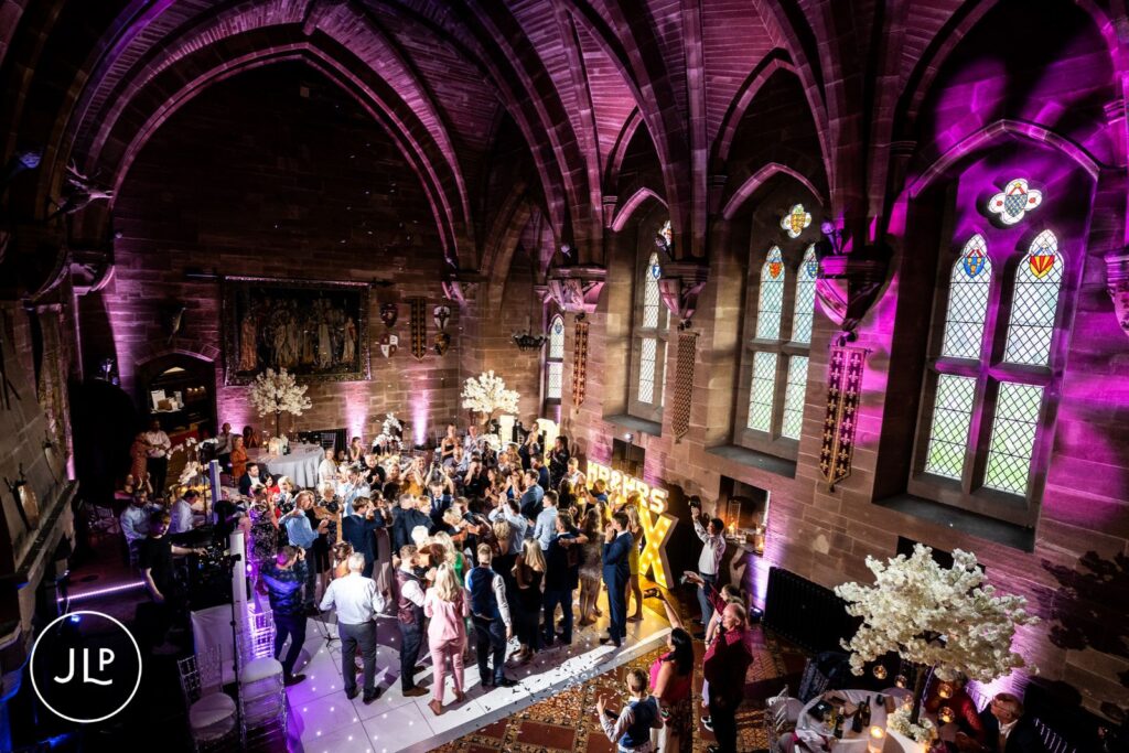 High-angle shot of a packed dance floor under pink lighting inside the grand hall at Peckforton Castle.
