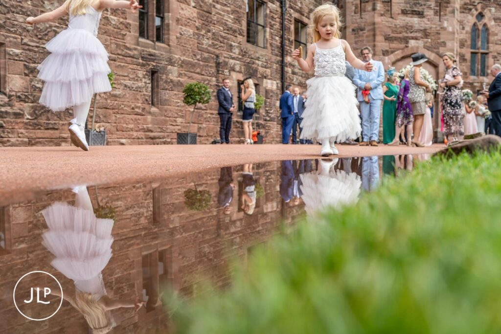 A creative reflection shot of young flower girls playing outside an elegant castle wedding venue.