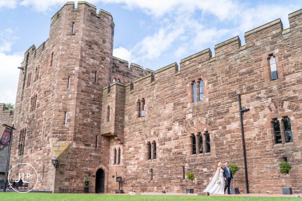 Wide shot of a couple outside the historic stone architecture, by a Peckforton Castle wedding photographer.