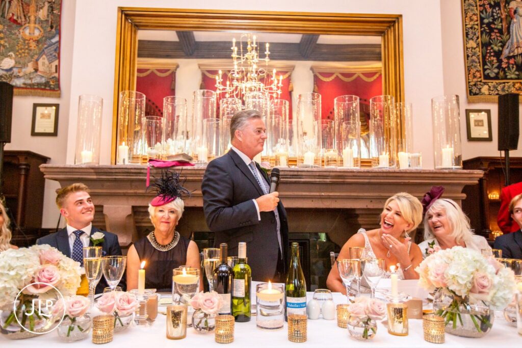 The groom giving a speech at the top table during an elegant castle wedding reception in Cheshire.