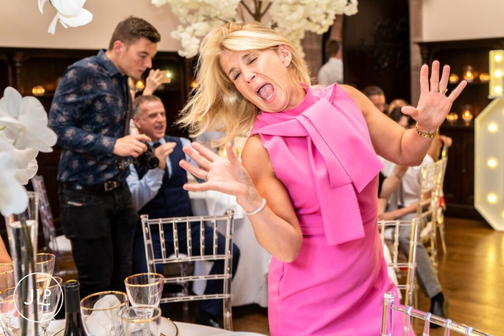 Candid wedding photography of a wedding guest in a pink dress dancing energetically at the reception table.