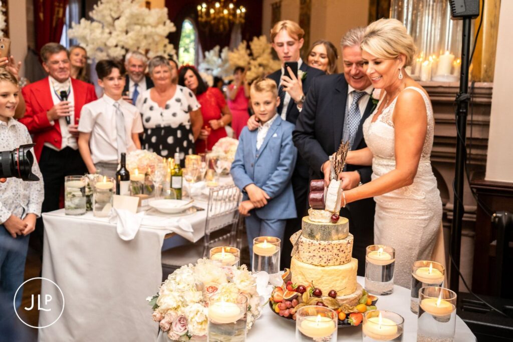 The newlyweds cutting a multi-tiered wedding cake made of cheese wheels, captured by a Cheshire photographer.