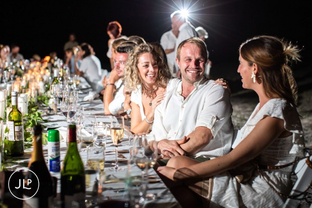 Candid safari wedding photography of wedding guests chatting and laughing at a long outdoor dining table at night.
