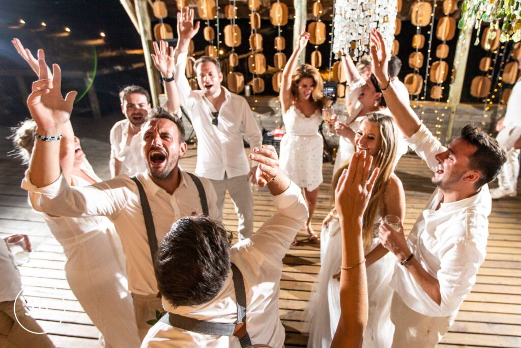 Candid safari wedding photography of a lively group of guests singing and cheering at a reception party.