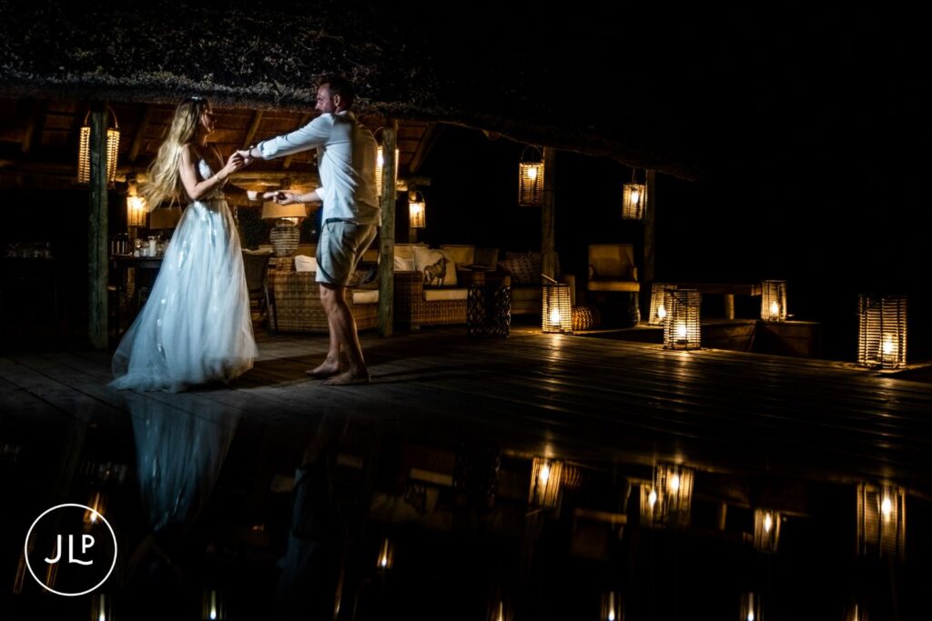 A bride and groom sharing a romantic night dance on a wooden deck lit by lanterns at a luxury safari lodge.