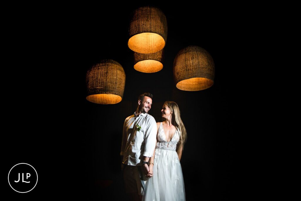 Dramatic backlit portrait of a couple holding hands beneath woven lantern lights, by an Africa wedding photographer.