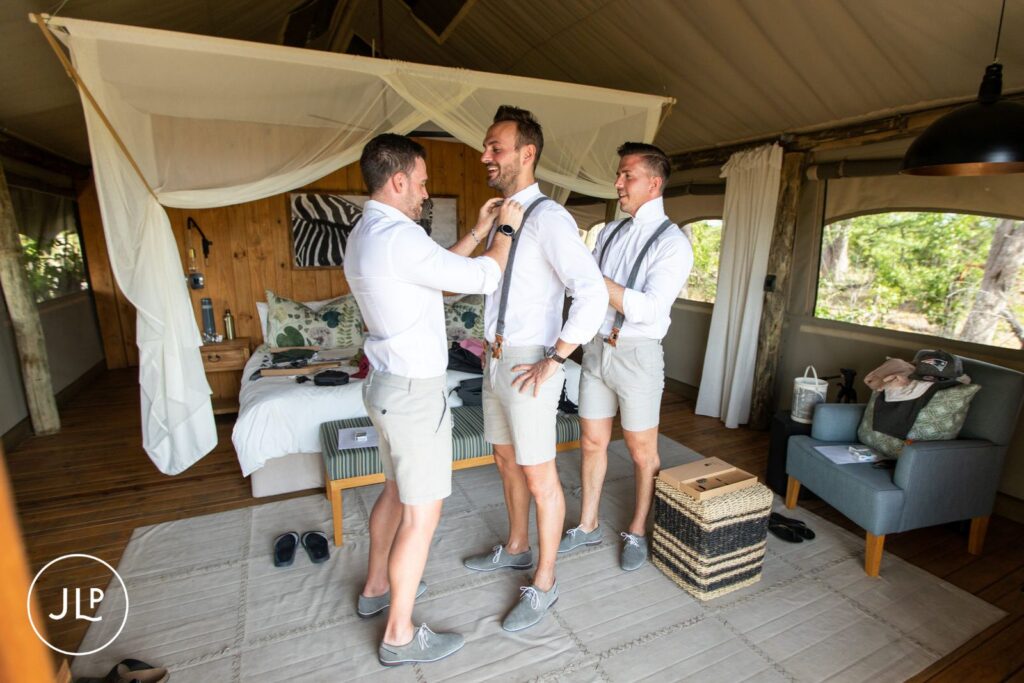 Natural wedding photography Botswana style of groomsmen helping the groom get ready inside a tented safari suite.