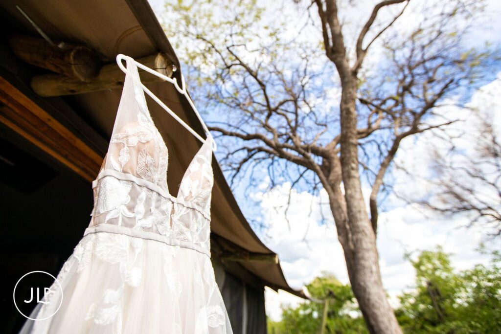 A beautiful lace wedding dress hanging outside a tented camp, captured by a safari wedding photographer Botswana.