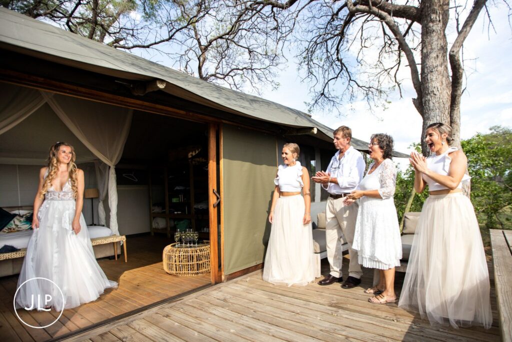 Candid safari wedding photography of the bridal party cheering as the bride steps onto the wooden safari deck.