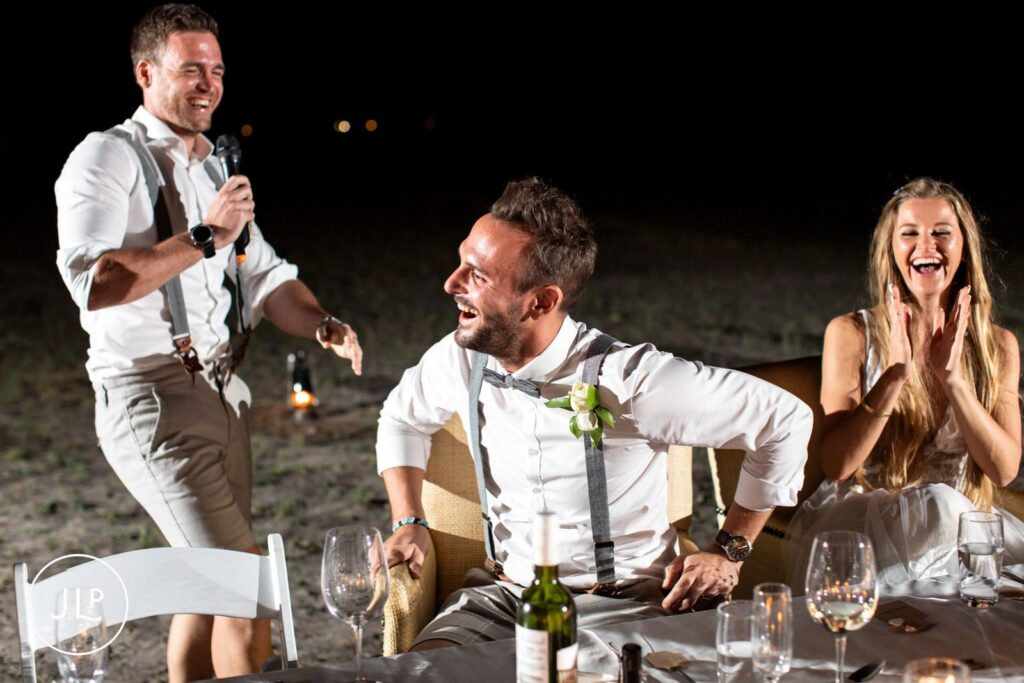 Natural wedding photography Botswana style of a groom laughing heartily during reception speeches in the bush.