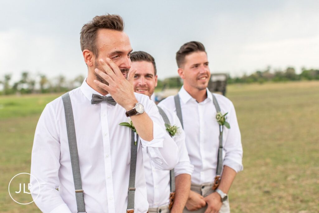 Natural wedding photography Botswana style of an emotional groom wiping away a tear at the altar.
