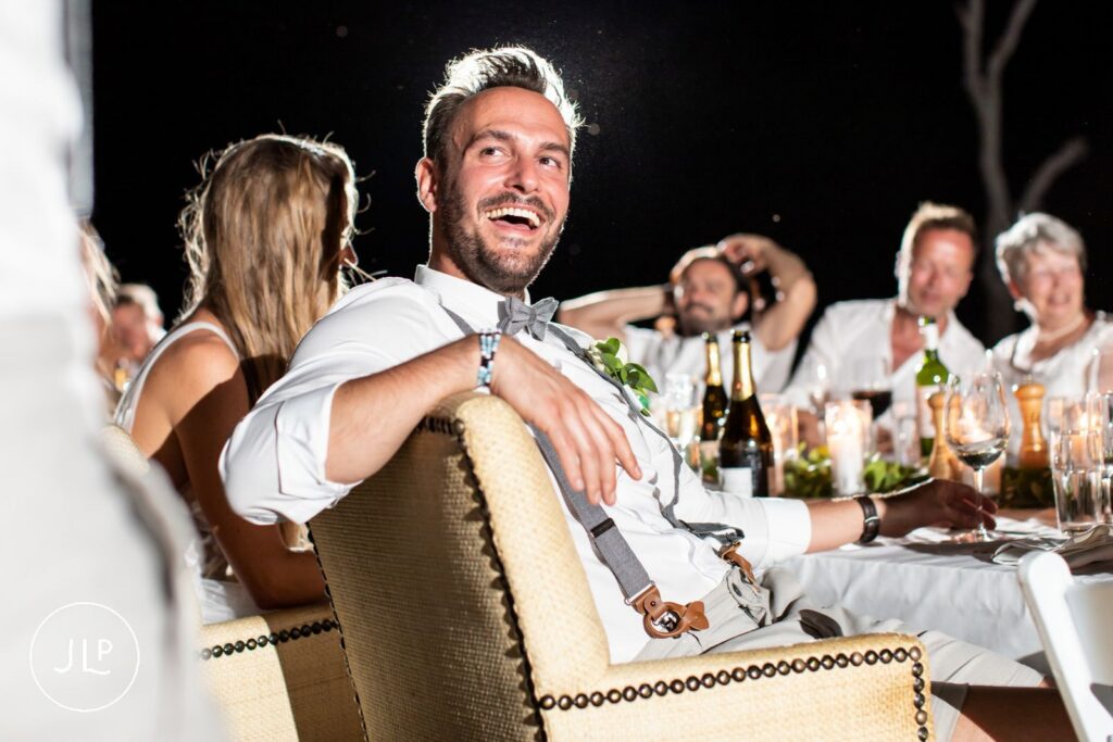 A happy groom smiling from his chair during his wedding dinner, captured by an Africa wedding photographer.