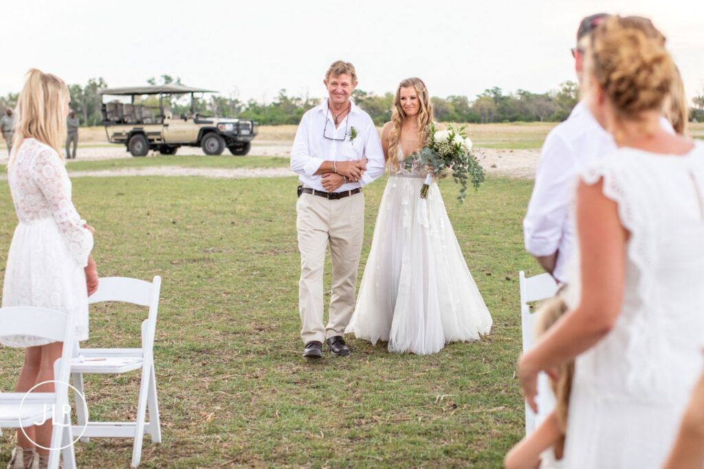 Botswana destination wedding photographer captures a bride walking down an outdoor aisle with her father.