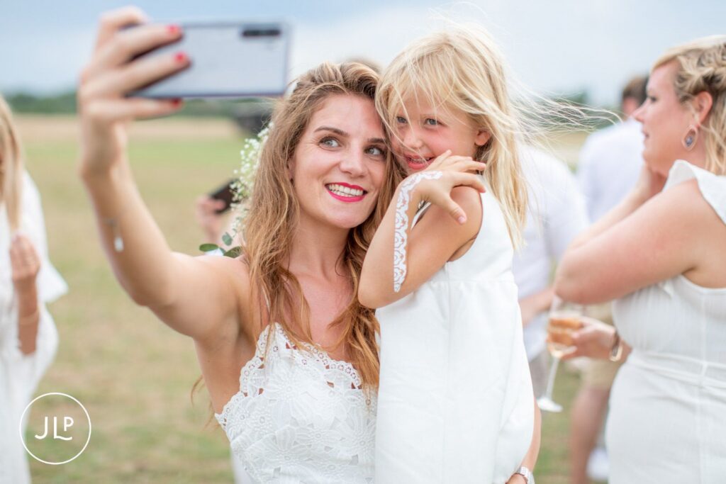 Candid safari wedding photography of a guest taking a joyful selfie with a young flower girl.