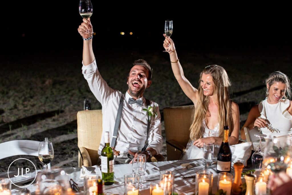 A bride and groom raising a champagne toast at their dinner table, by a Botswana safari wedding photographer.