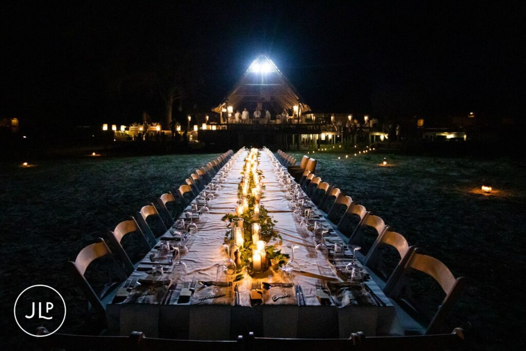 Wide shot of a long candlelit dining table set up outdoors for a luxury safari wedding Botswana reception.