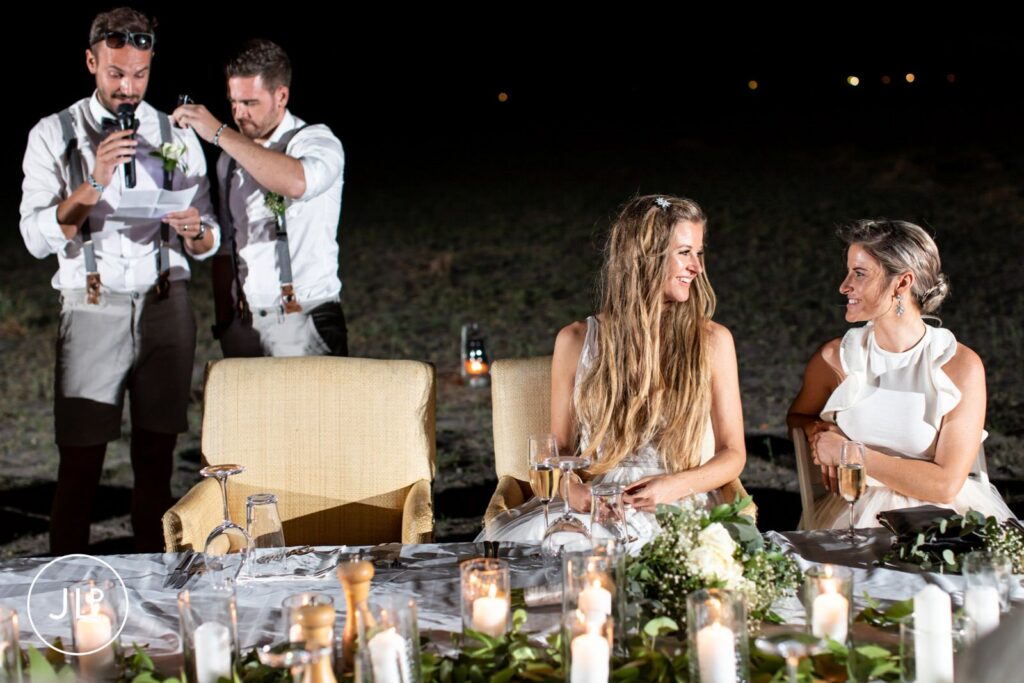A bride smiles at her bridesmaid during reception speeches, captured by an Africa wedding photographer.