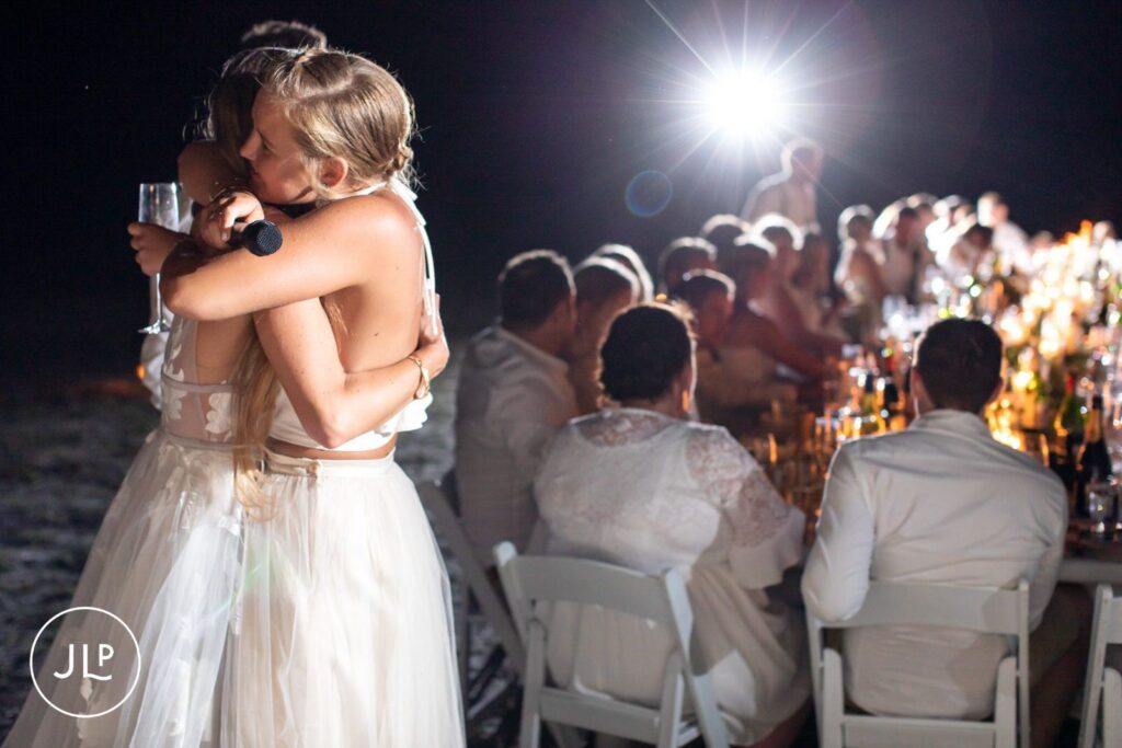 Candid safari wedding photography of an emotional embrace between the bride and a guest next to the dinner table.