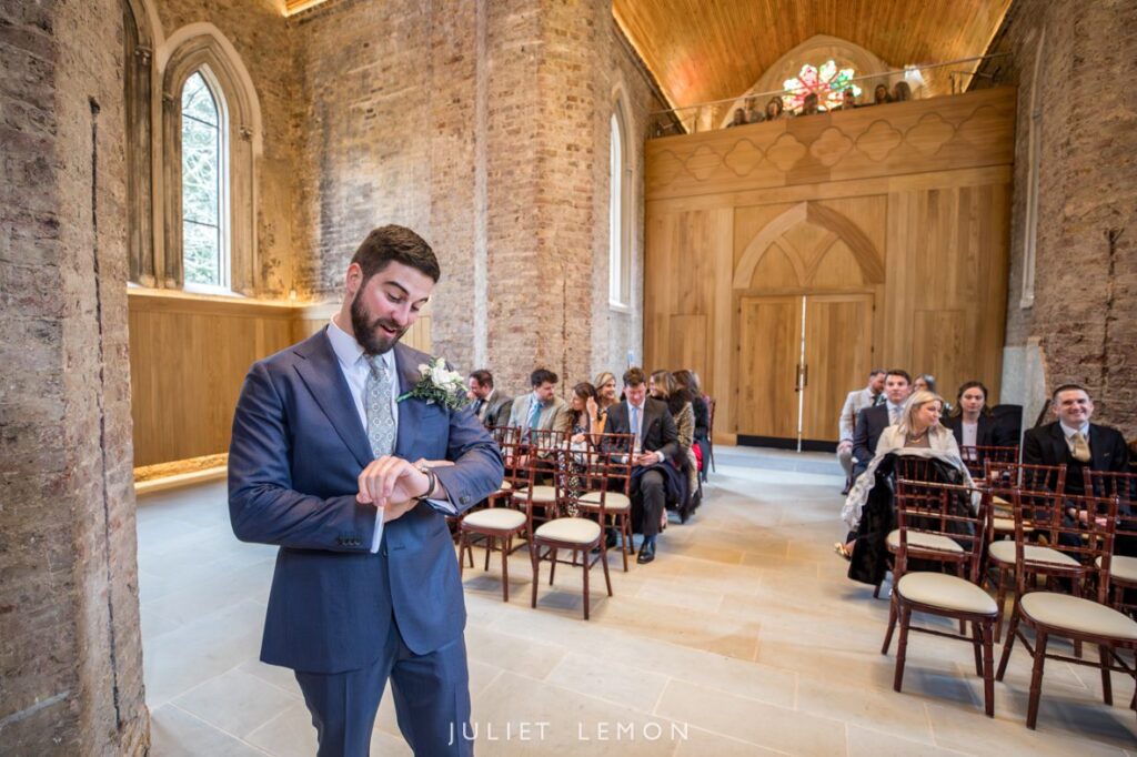 patient groom standing by the alter in the chapel checking the time on his watch, waiting for his bride