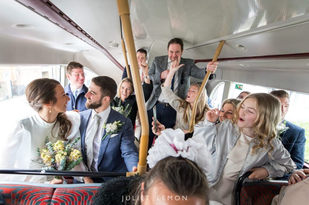 bride and groom with their wedding guests on the top deck of double decker red London bus in stoke newington