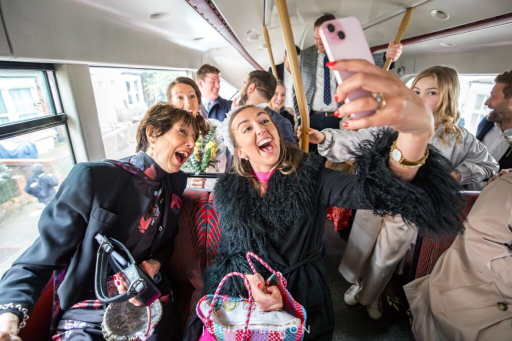 Candid wedding photography London: wedding party taking a joyful selfie on a red double-decker bus.