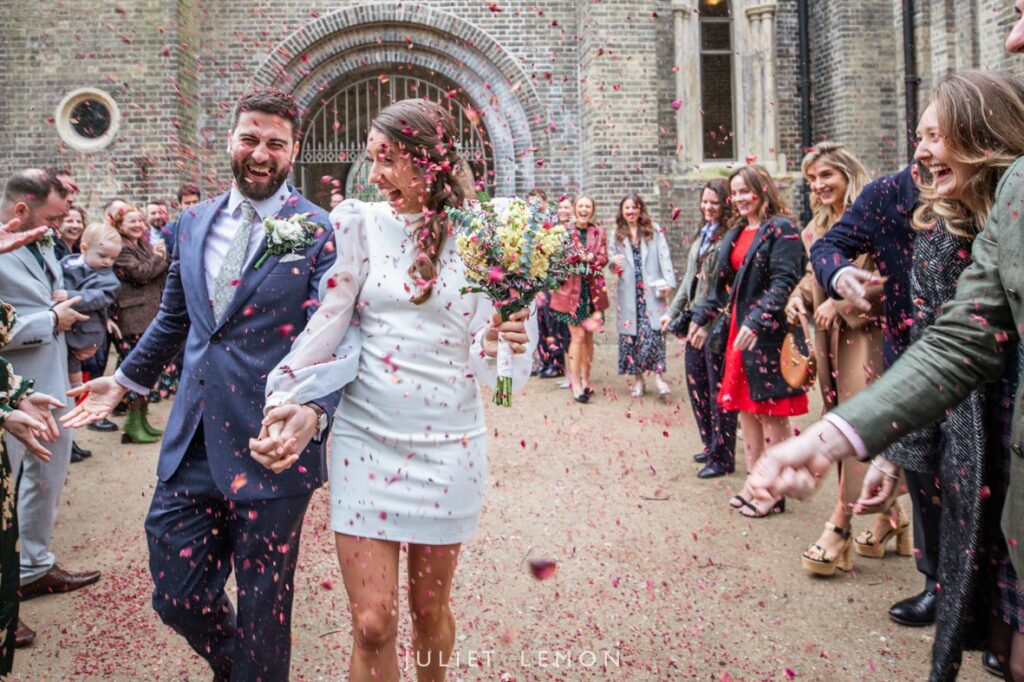 Confetti rains down on the smiling couple as they walk under the chapel archway