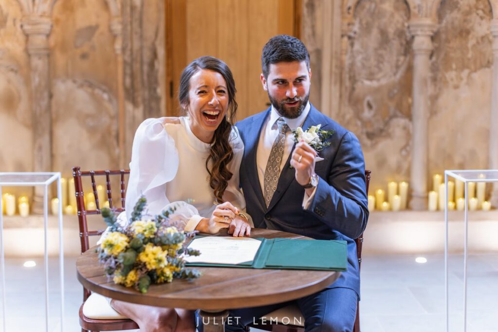 Abney Park Chapel wedding photography of the bride laughing while signing the marriage register during the ceremony.