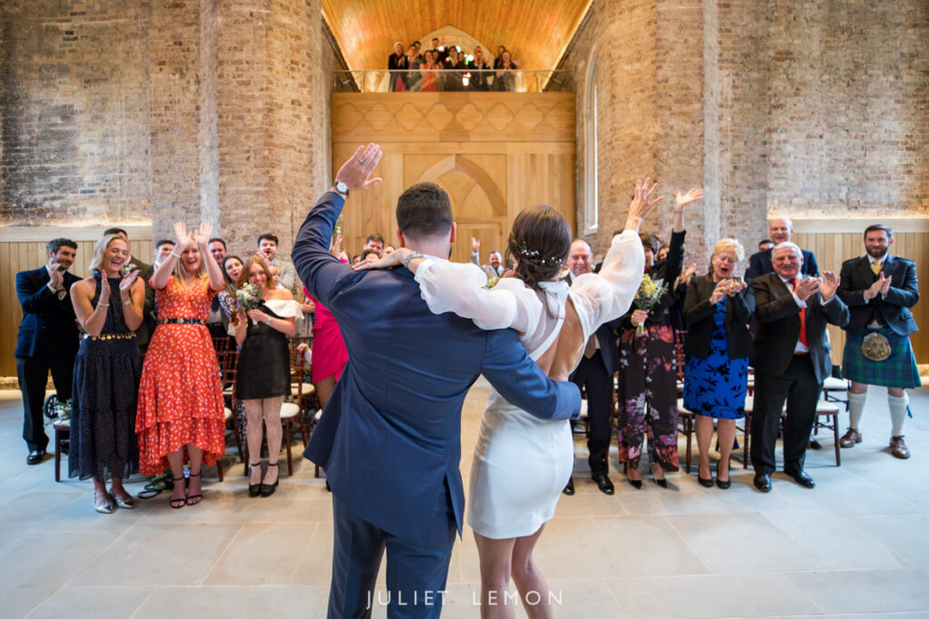 Back view of the happy couple walking down the aisle hand-in-hand, cheered by guests