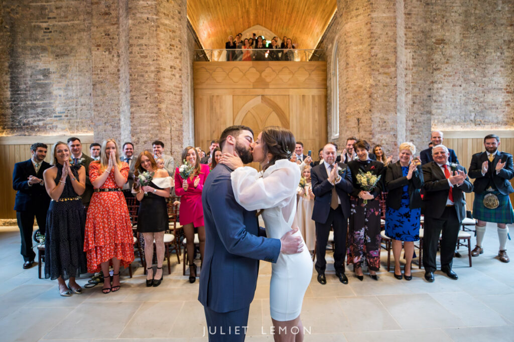 The couple shares a first kiss, captured by an Abney Park Chapel wedding photographer as guests applaud.