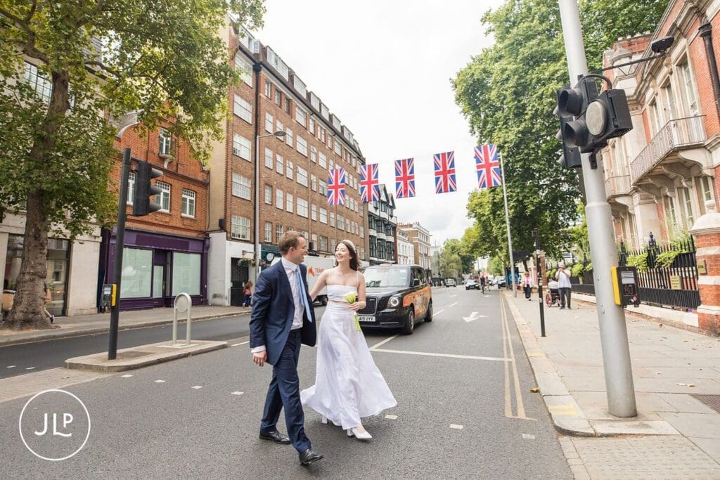 Bride and groom holding hands while crossing a London street during their Chelsea registry office wedding.