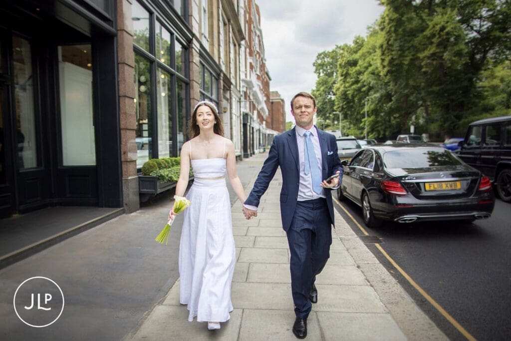 Newlyweds holding hands and walking down a London street after their Chelsea registry office wedding.