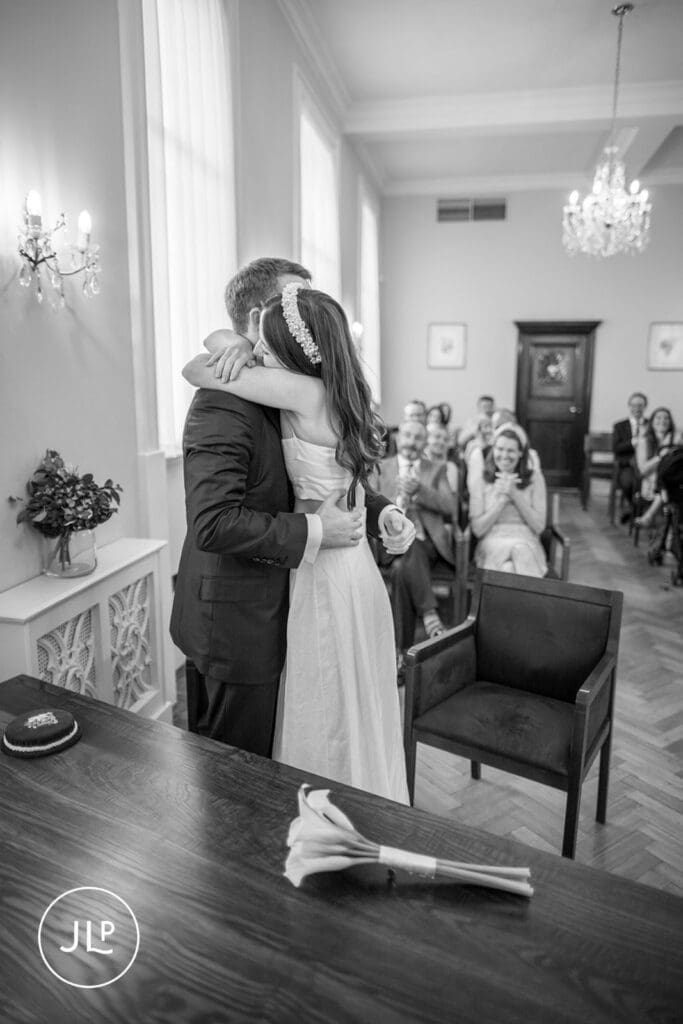 Bride and groom holding hands and smiling during a ceremony at Chelsea Town Hall wedding venue in London.