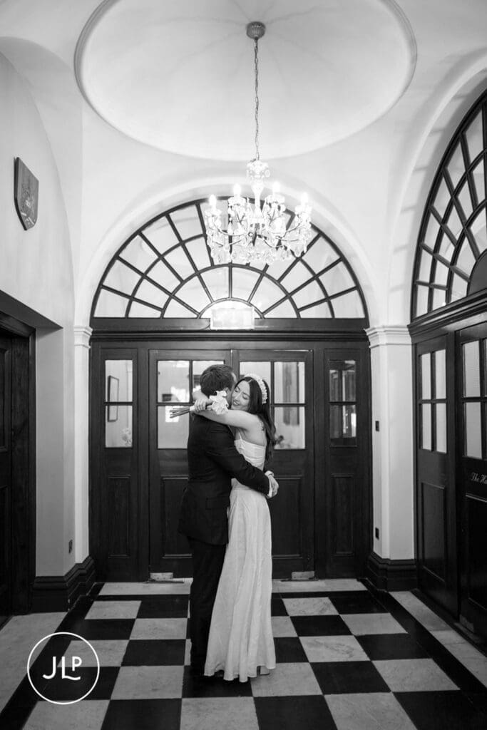 Black and white shot of newlyweds hugging in the tiled foyer, by a Chelsea Old Town Hall wedding photographer.
