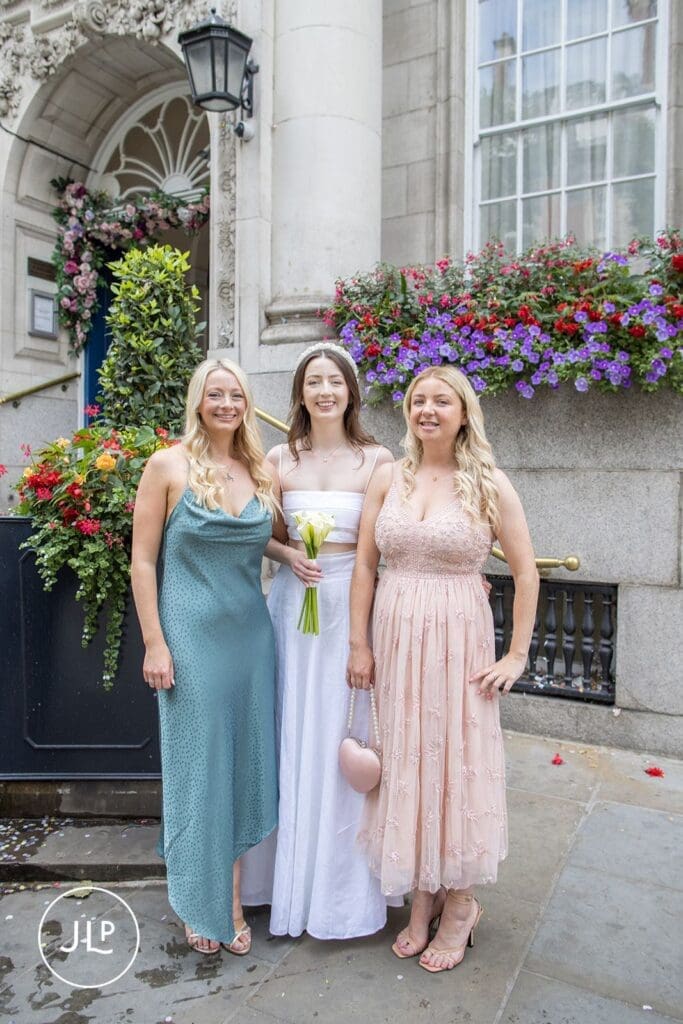 Smiling bride posing with bridesmaids outside the Chelsea Town Hall registry office wedding venue.