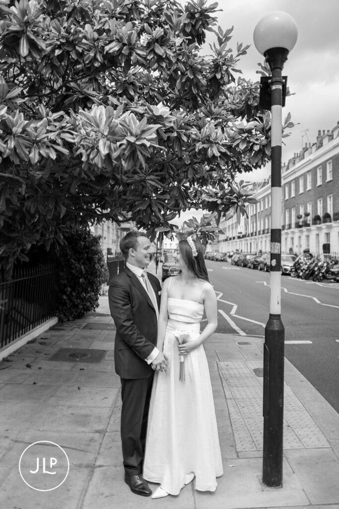 B&W portrait of newlyweds standing by a street lamp, captured by a London intimate wedding photographer.