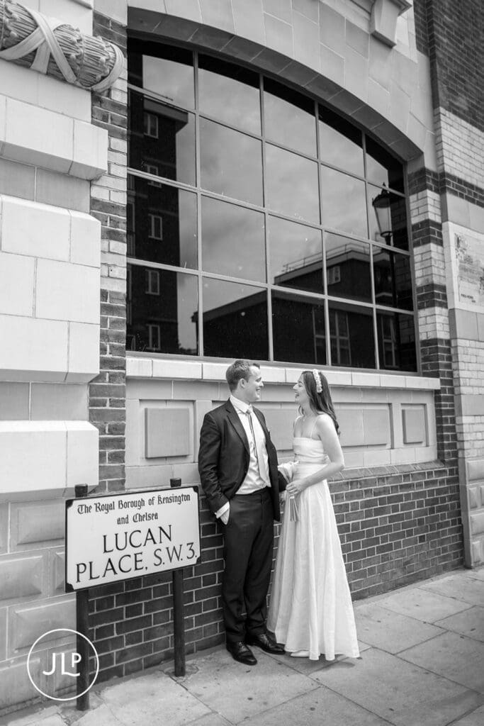 B&W photo of a bride and groom posing next to a Lucan Place street sign during a Chelsea wedding day.