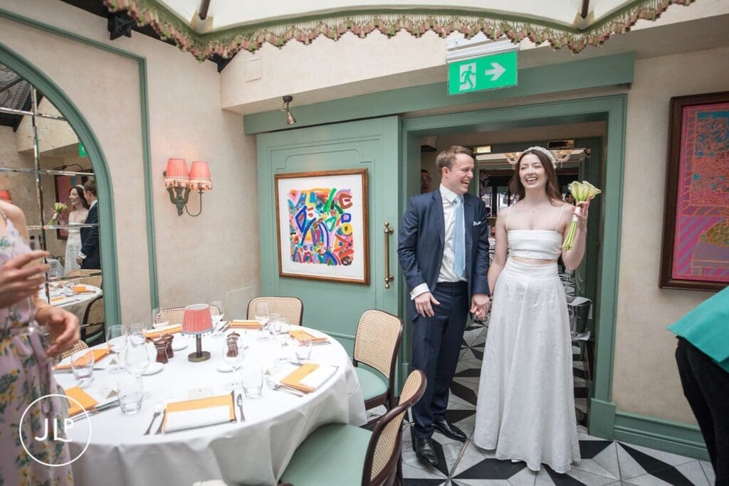 Laughing newlyweds entering their stylish dining room reception after a Chelsea Town Hall wedding.