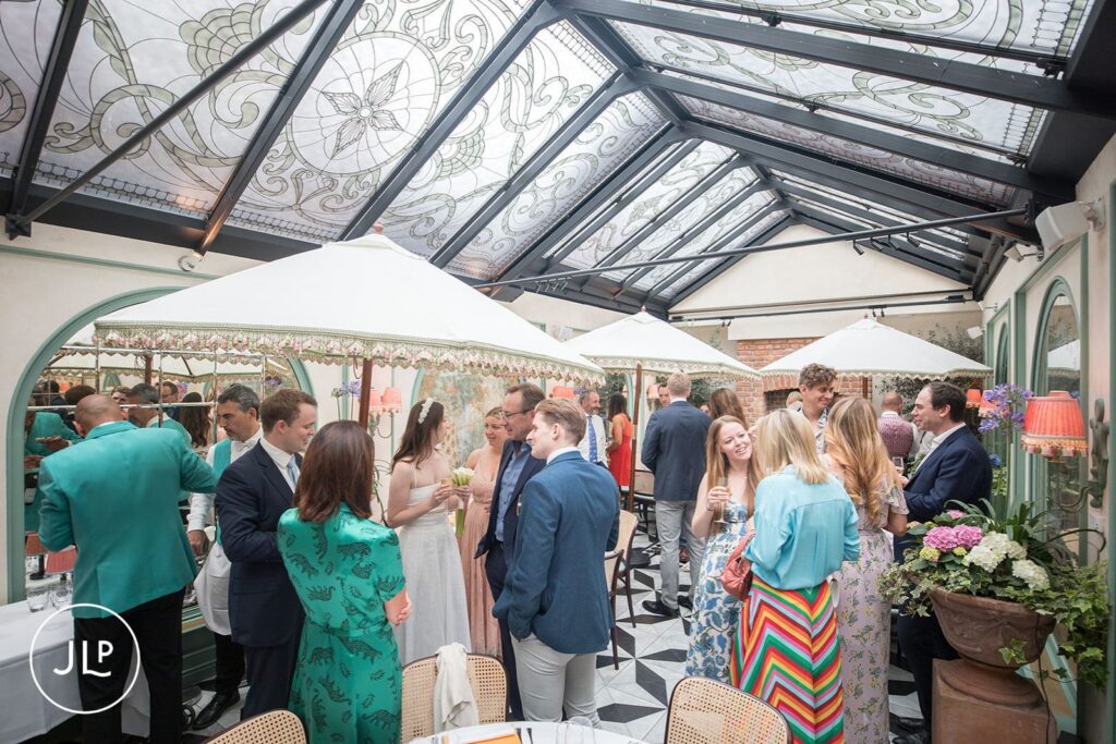 Guests mingling in the stunning glass-roofed conservatory during an intimate London wedding reception at Daphne's.