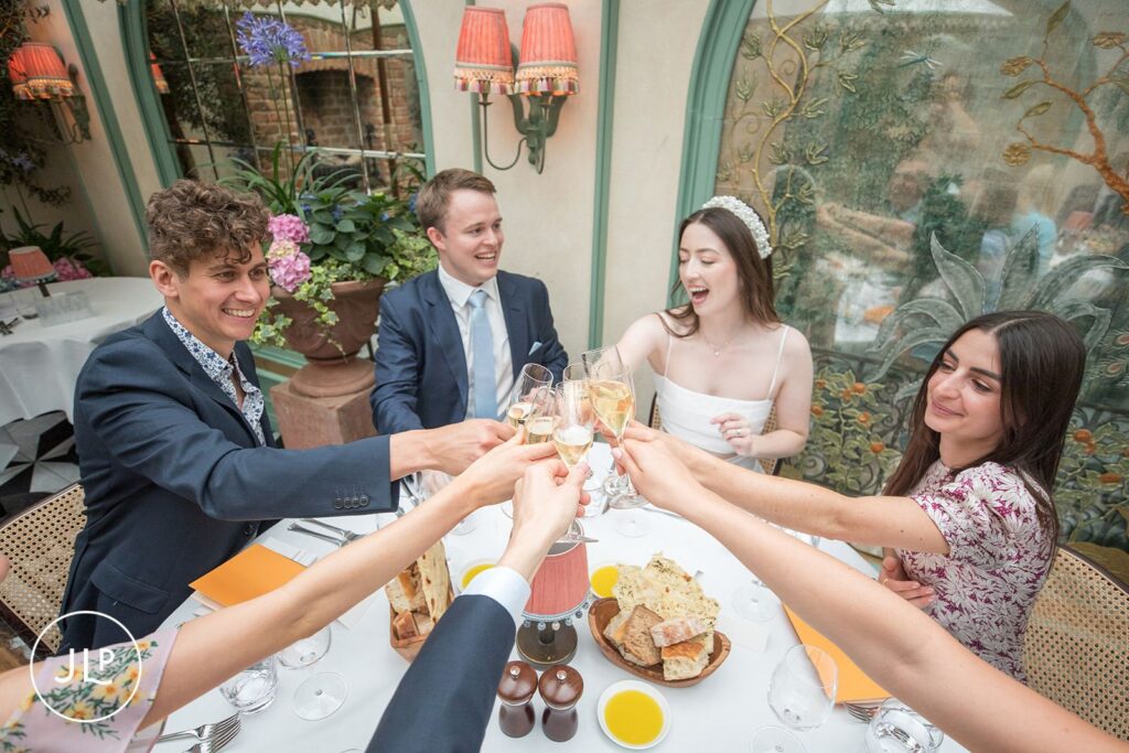 Newlyweds and guests sharing a joyful toast during a Daphne’s Chelsea wedding breakfast.