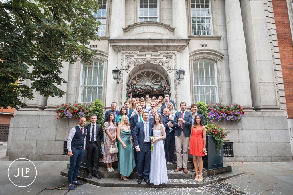 Wedding party group photo on the steps of Chelsea Old Town Hall in London.