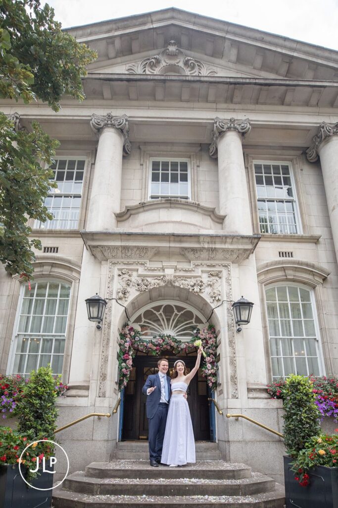 Joyful bride and groom celebrating on the steps of their Chelsea Old Town Hall wedding.