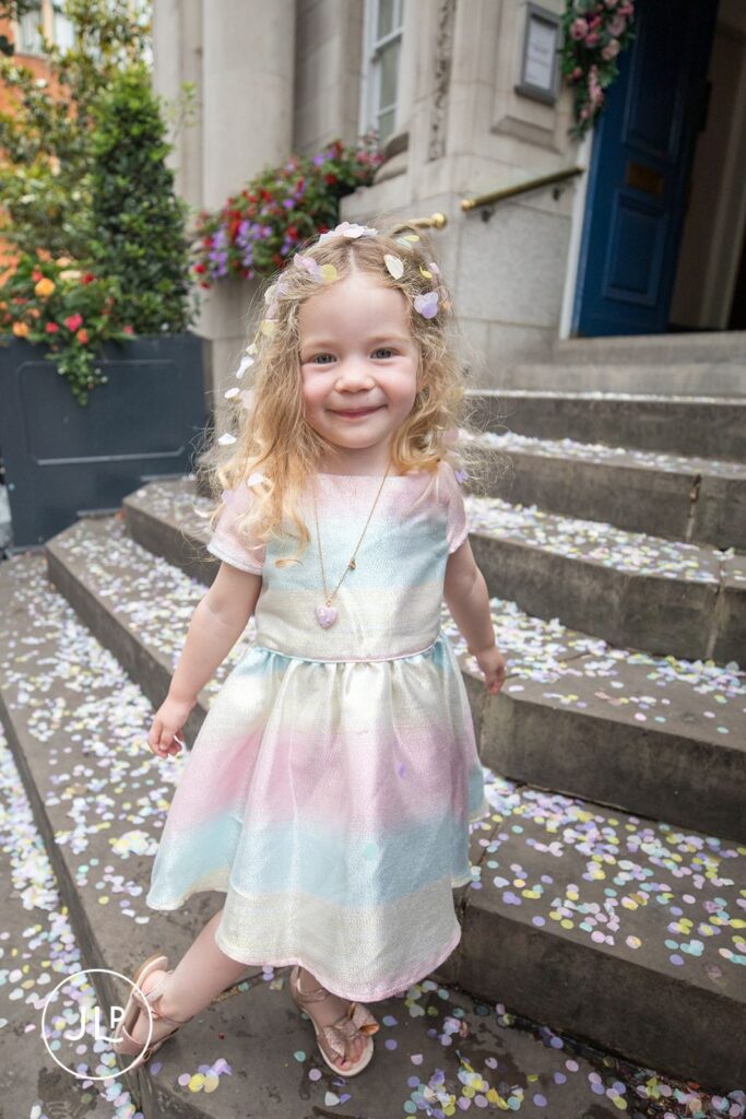 Flower girl in a rainbow dress on the confetti-covered steps of Chelsea Old Town Hall.
